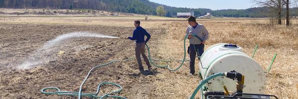At a test site for the direct seeding project at the Hubbardton River Clay Plain Forest in Benson, Vermont, two crew members from The Nature Conservancy use a hydroseeder to spread seed in April 2021. Two people in a farm field using a sprayer